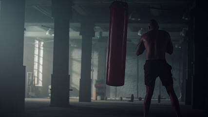 Muscular man boxing punch bag. Male boxer doing cardio workout in sports club