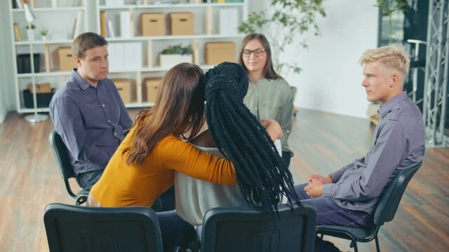 Young Mixed-race People Hug Each Other For Support, Comfort, Help with a Psychological Problem During a Group Therapy Session. The Concept of Psychological Recovery, Compassion and Empathy.