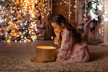 Merry Christmas! Beautiful girl with magic gift at home near Christmas tree and fireplace
