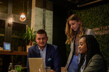 Cheerful work colleagues working on a laptop while having a meeting in a cafe