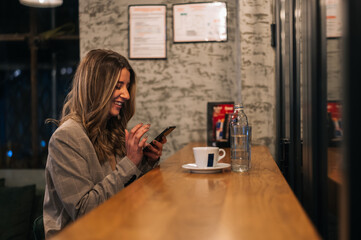 Young beautiful woman using smartphone while drinking coffee in a cafe