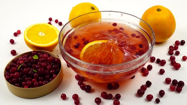 Slice of a fresh orange fall into a glass bowl with non-alcoholic fruit and berry punch slow motion.  