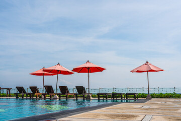 Red umbrella and sun beds at resort and tropical sea with swimming pool for holiday vacation