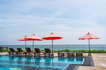 Red umbrella and sun beds at resort and tropical sea with swimming pool for holiday vacation