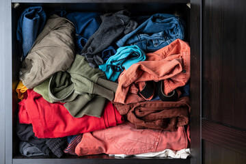 Variety of brightly colored clothes lie casually on a shelf in a closet. 