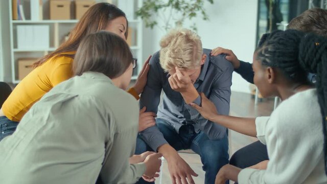 A Group Of People Sitting in a Circle During a Group Therapy Session. The Young Guy Sharing Emotional Pain While Receiving Psychological Help From Mixed-race People. Alcohol Dependence, Depression.