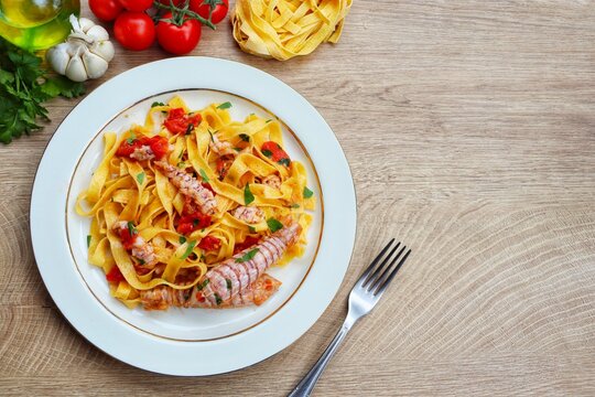 Italian Traditional Dish"Fettuccine con le canocchie",fettuccine pasta with mantis shrimps cherry tomatoes,olive oil,garlics,white wine,parsley and peppers on plate with wooden background.Top view