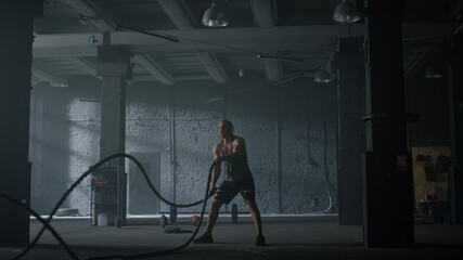 Bodybuilder training with battle ropes. Man performing strength exercises 