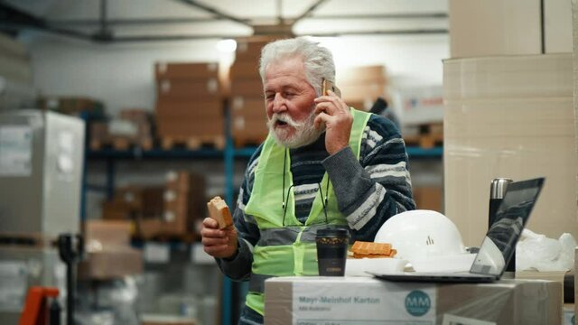 Old warehouse supervisor talks on the phone during a breakfast break