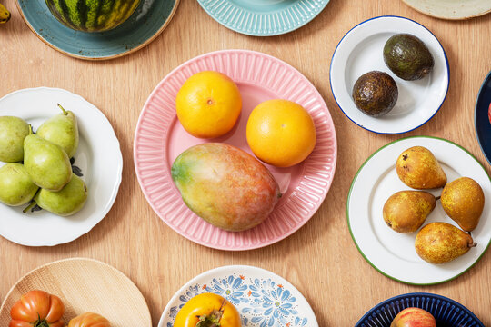 Top view image of plate set with assorted fruits, watermelon, grapefruit, African mangoes, ripe avocados, pink tomatoes, pears and bananas