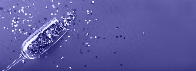 Champagne glass with star shaped sequins on a blue background. Very Peri color of the year