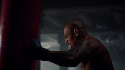 Obraz na płótnie Canvas Angry man hitting punching bag. Sportsman training punches in sport club