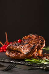 Grilled cuts of meat, hot smoky steak on a slate stone table. Black cutlery. Side view. Vertical position.