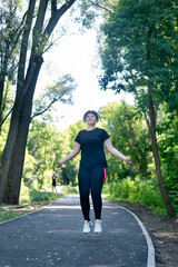 Young woman in activewear choosing healthy lifestyle. Girl with excess weight jumping rope in the park.