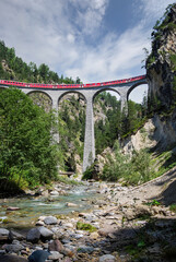 Fototapeta na wymiar Train of the Rhaetian Railway over the famous Landwasser Viaduct. This viaduct is located in the Albula railway line just before the town of Filisur in the Swiss canton of Graubünden.