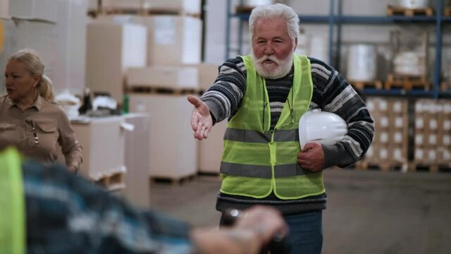 Angry boss shouting at workers, shows delivery delay  to the warehouse.  Frustrated elderly foreman yells at the storekeeper for poor work in the factory
