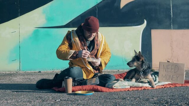 A tramp and his dog are eating in city the street