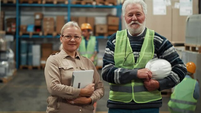Portrait of Old warehouse worker and a mature female supervisor pose and look at the camera