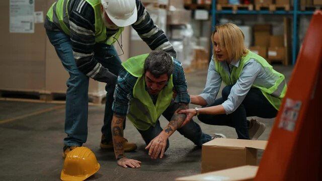 Colleagues help a worker lying down after an accident at the warehouse. Workers getting hurt and accident on the job. Male worker falling down in warehouse