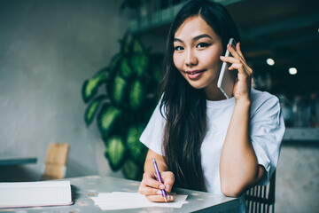Cheerful woman talking on phone and writing notes