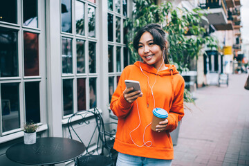 Optimistic Asian woman with earphones messaging on smartphone