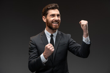 Portrait of ecstatic overjoyed handsome man expressing winning gesture with raised fists and screaming, celebrating victory isolated on black background
