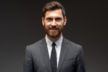 Portrait of happy good looking businessman in formal suit smiling to the camera in front of black wall background. Stock photo