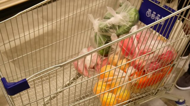 the customer puts a bag of vegetables into the grocery cart and rolls the cart further.grocery trolley driving through the store. High quality 4k footage