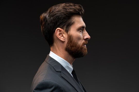 Profile view of self confident bearded man looking with serious expression, unsmiling determined business man. Indoor studio shot isolated on black background
