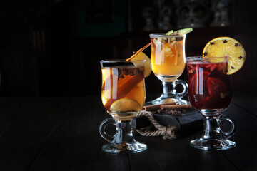 Mulled wine in glass glasses. Three types of mulled wine. Assorted drinks on a dark background. A hot traditional cocktail of red wine and fruits. Healthy winter drink.Side view.Copy space.