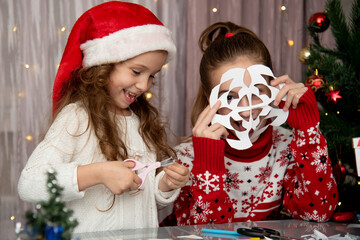 Two cute sisters cut snowflakes out of paper, preparing for the holiday. New Year. Christmas. Comfort.