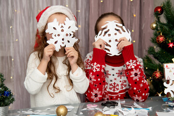 Two cute sisters cut snowflakes out of paper, preparing for the holiday. New Year. Christmas. Comfort.