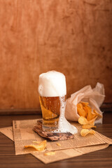 A glass of beer and chips. A glass of beer on a wooden background. A glass of beer with foam.