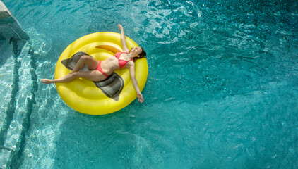 Young sexy blonde woman in pink Bikini on smily air mattress, floating relaxing in the pool,...