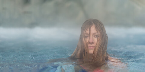 Pretty blond woman portrait in pink bikini relaxes in thermal bath hot water pool in hot steam