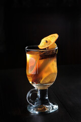 Mulled wine based on white wine. A cocktail of white wine, fruits and spices. Drink in a glass goblet on a black background. A hot drink for health. Vertical photo. Side view.