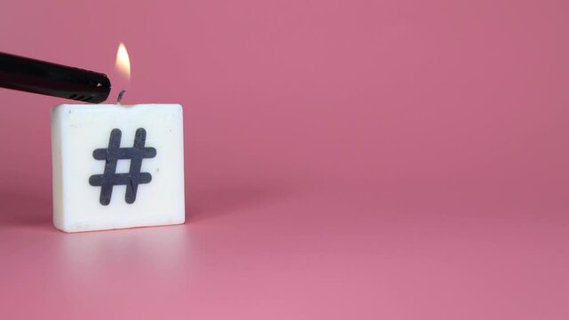 A square candle printed with a hash tag being lit and blown out on a pink background