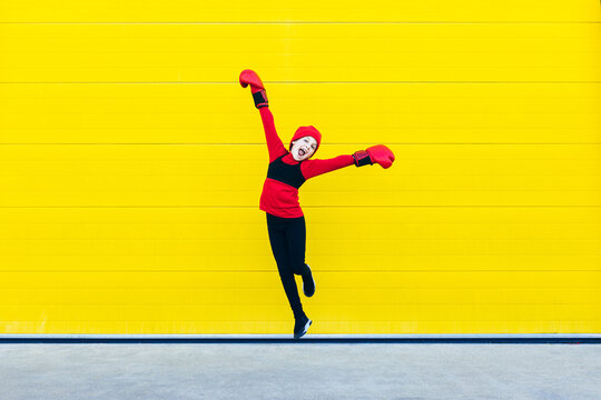 Excited girl in boxing gloves jumping against colorful wall