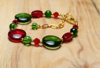 Handmade bracelet in Christmas color made of glass beads on a wooden table, New Year's composition, New Year's gifts, selective focus, horizontal orientation.