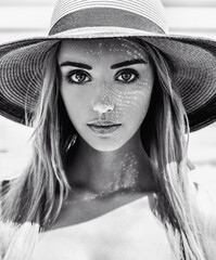 Black and white close-up portrait of a young beautiful caucasian girl with a pretty face and big eyes wearing a hat on a warm summer day.