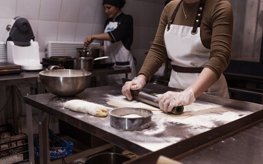 a female chef rolls out dough with a metal rolling pin in the kitchen in a restaurant. beautiful lighting