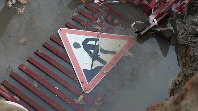 A road fence and roadworks sign fell into a pit filled with muddy rainwater.