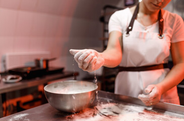 a female cook sprinkles flour on a metal table in the kitchen before making dough. close-up