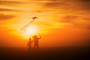 Fototapeta na wymiar Flying a kite. Girl and boy fly a kite in the endless field. Bright sunset. Silhouettes of people against the sky.