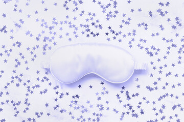 Color of the year 2022 very peri. Satin eye sleeping mask and silver stars confetti on light background. Sweet dreams, trendy colors concept. Copy space, flat lay. Accessories for women