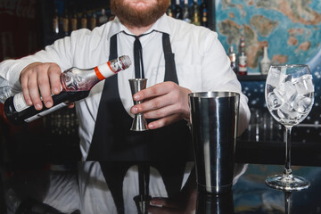 The hands of a professional bartender pour red syrup into a measuring glass of jigger, next to a...
