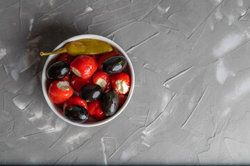Delicious Italian appetizer, red bell pepper stuffed with cheese cream, herbs, black olives and hot peppers on a gray background