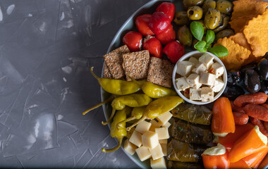 Plate with various party snacks and antipasti on a gray background, top view