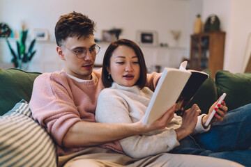 Man and woman with smartphone read book on sofa