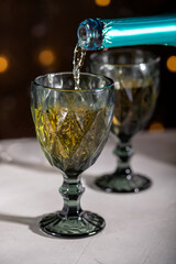 The concept of a festive New Year's Christmas card. Two glasses with sparkling wine against the background of multi-colored garland lights. Close-up, Selective focus, copy space, low key